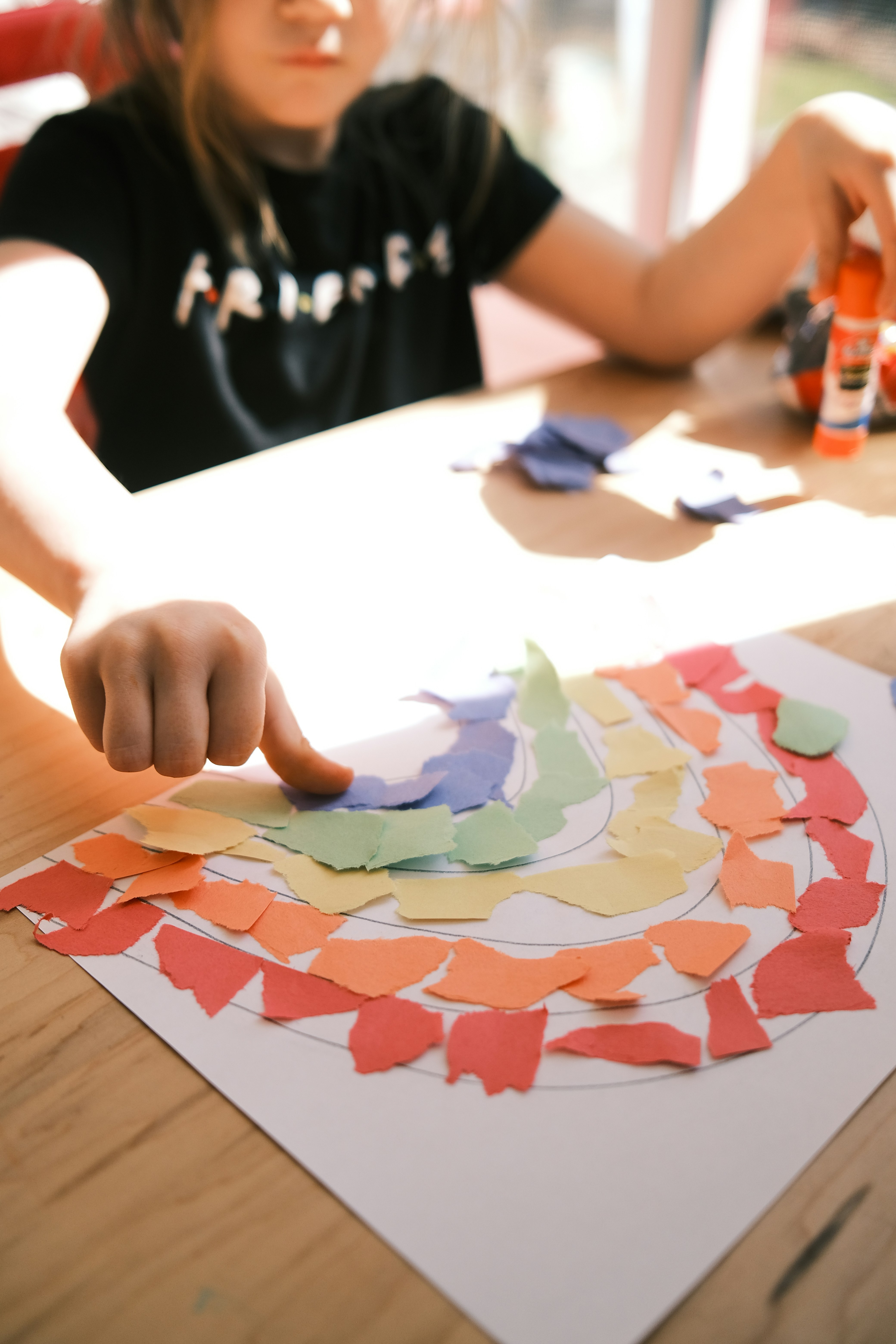 Child creating a paper rainbow art project at a table.